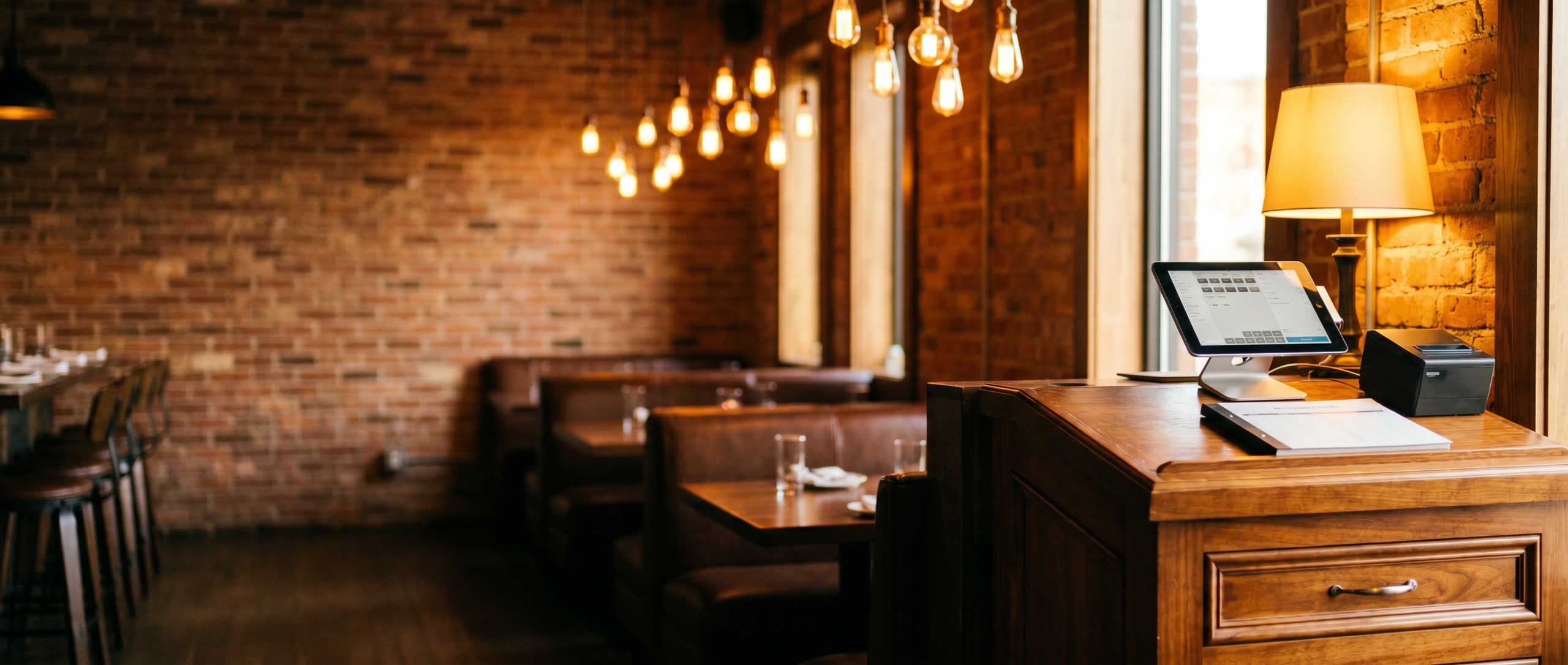 A warm restaurant interior with a host stand and POS terminal on the right